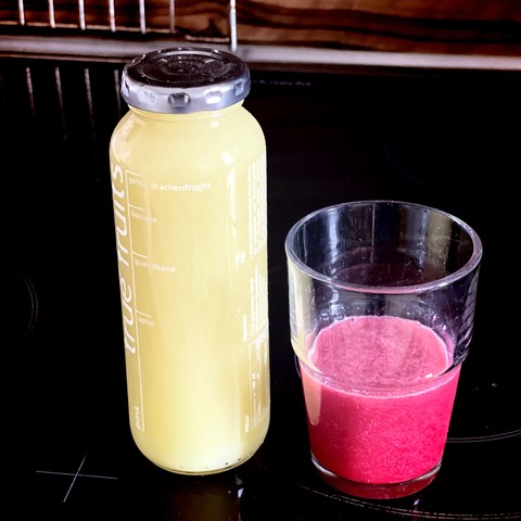 A bottle of fruit juice next to a glass with a pink beverage on a dark surface.