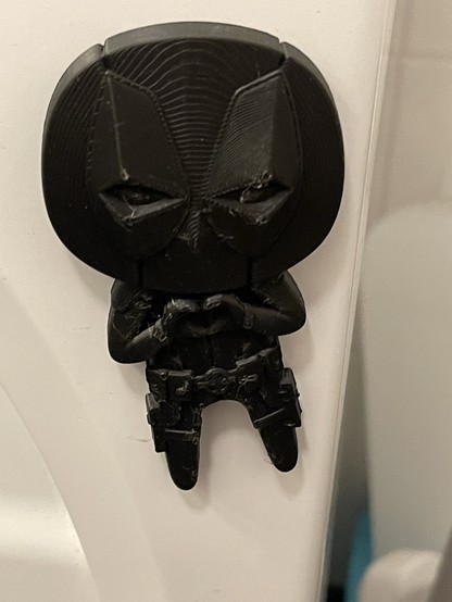 3D printed Deadpool fridge magnet in black filament. Attached to a white surface. 