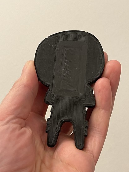 The plain back of a black 3D printed Deadpool figurine fridge magnet. In the middle a square can be seen in the pattern of the filament layer. 