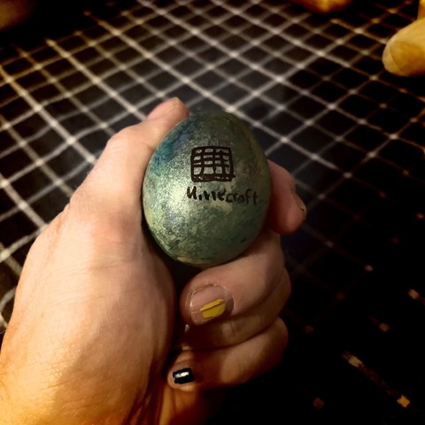 A hand holding a dyed egg with the word "Minecraft" and a logo on it.