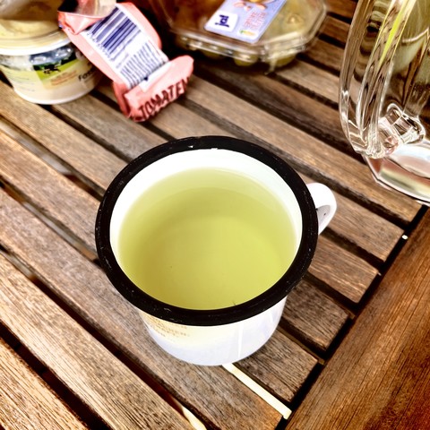 A cup of light green peppermint tea on a wooden table with some packaged food items and a glass jug in the background.