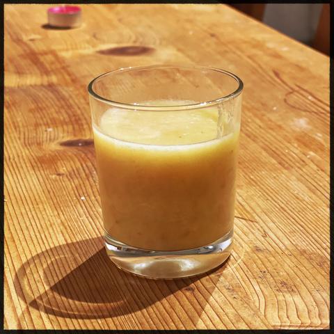 A glass filled with yellow cloudy juice. A mix of Lemmon , banana and ginger. The glass is placed on a wooden table. 