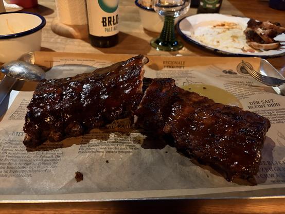 Two racks of ribs on a paper-lined tray, next to a beer bottle and a plate with food remnants.