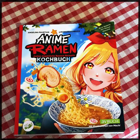 A colorful cookbook cover features an anime girl with a bowl of ramen, surrounded by floating ingredients, on a red and white checkered cloth. The book cover reads: Anime Ramen Kochbuch