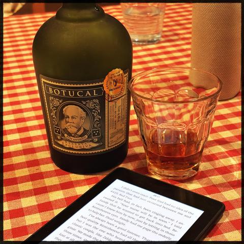 A bottle of Botucal rum, a glass of amber liquid, and a tablet on a red and white checkered tablecloth.