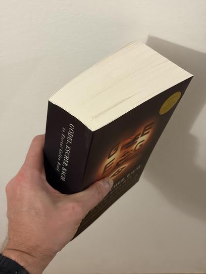 A person holding a black book with gold text and a yellow sticker on a white surface.