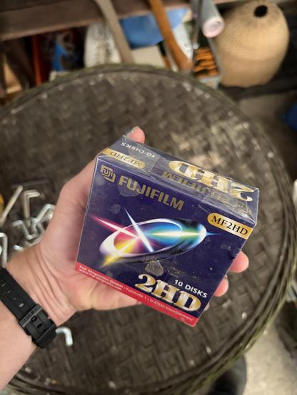 A person holding a box of Fujifilm 2HD MF2HD magnetic 3,5" disks in front of a circular old table