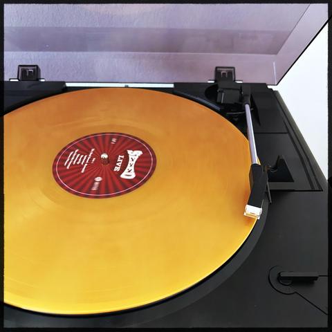 Ein gelber Vinylrekord auf einem schwarzen Plattenspieler mit einem roten Etikett und einem silbernen Tonabnehmer.Seeed Live Album