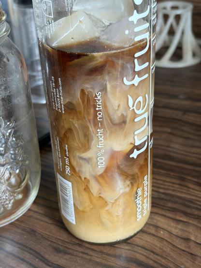 Clear bottle with cold brewed coffee and milk not yet fully mixed and ice cubes on a wooden surface.
