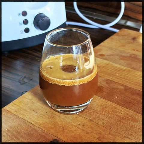 A small glass with espresso. Creamy top. Sits on a wooden board