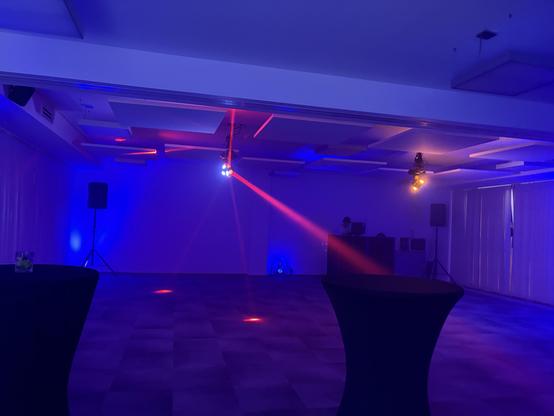A room with purple and red lights, a DJ booth, and two black tables. Looks like a disco but nobody is dancing.