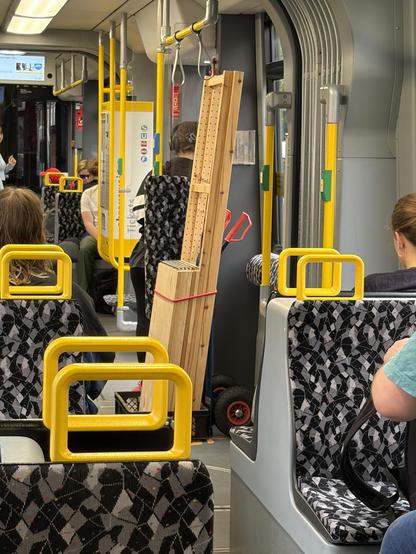 Eine Tram in Berlin mit einem Transportkarren mit Holzplatte und Holzlatten und Passagieren. Die Sitze haben ein schwarz-weißes Muster und gelbe Griffe.