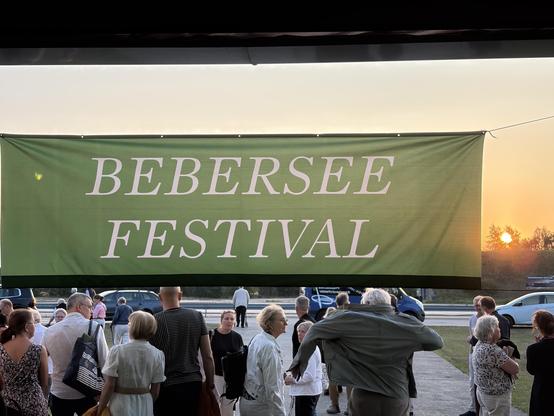 Grünne Fahne mit weißer Schrift "Beberssee Festival" über einer Menschenmenge bei Sonnenuntergang.