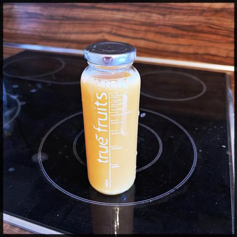 A small bottle filled with ginger/lemon/honey juice. It's got a silver metal lid and sits on a black stovetop. There is a brand name on the bottle vertically: true fruits. 
But the contents is actually self made. I'm just reusing the bottle. 