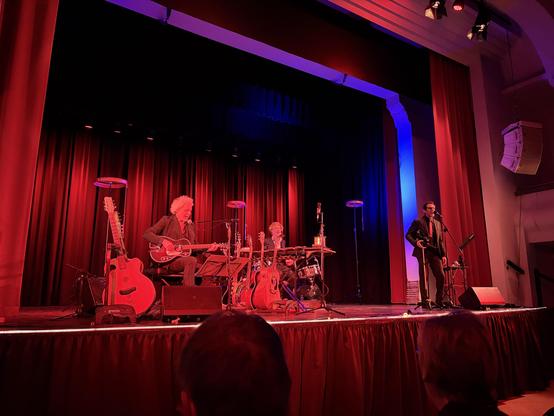 Auf der Bühne des "Club der toten Dichter" performt das Trio ihr Programm "Galgenlieder" – eine musikalische Neuvertonung der Gedichte von Christian Morgenstern. In rot-blaues Bühnenlicht getaucht sitzt links Reinhardt Repke (Gitarren, Gesang) mit lockigem grauem Haar in gestreiftem Anzug und spielt Gitarre, in der Mitte spielt Markus Runzheimer (Bass, Perkussion, Gesang) am Xylophon/Glockenspiel. Rechts steht Hans-Werner Meyer (Gesang, Geige) im dunklen Anzug am Mikrofon und singt.

Um die Mus…